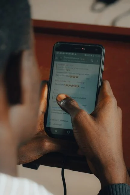 Hands using smartphone beside laptop with stock charts, showcasing digital trading.